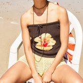 Person wearing a strapless top with a pie design and yellow shorts on a beach chair.